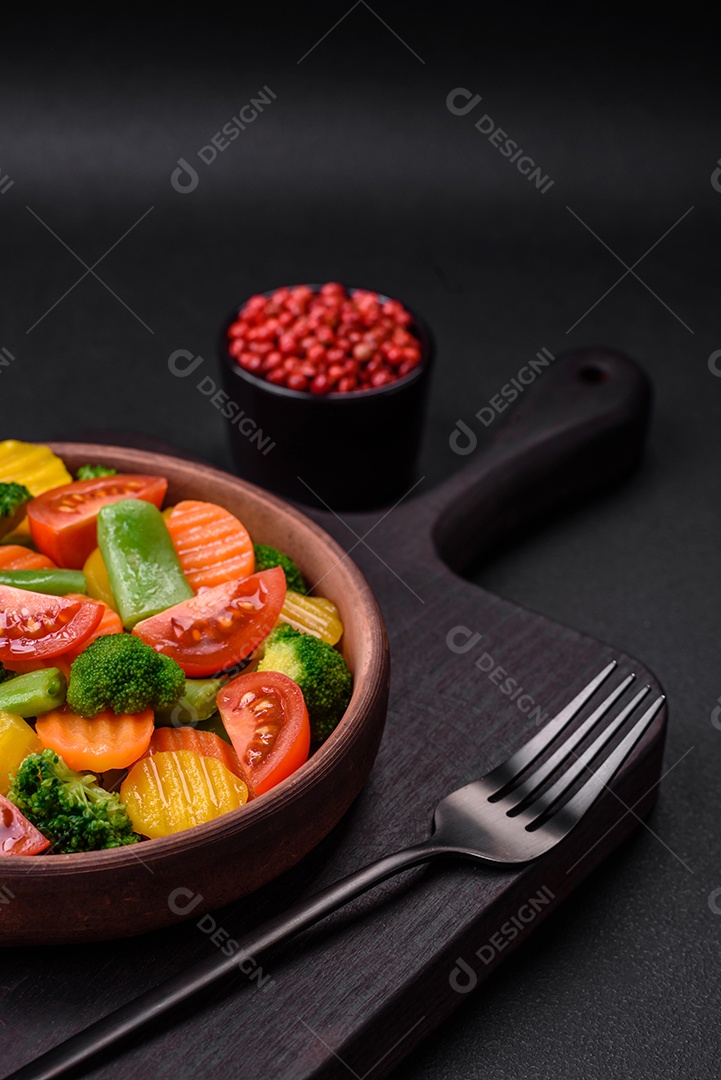 Salada de legumes frescos e cozidos no vapor, tomate cereja, brócolis, cenoura e feijão de espargos sobre um fundo escuro de concreto