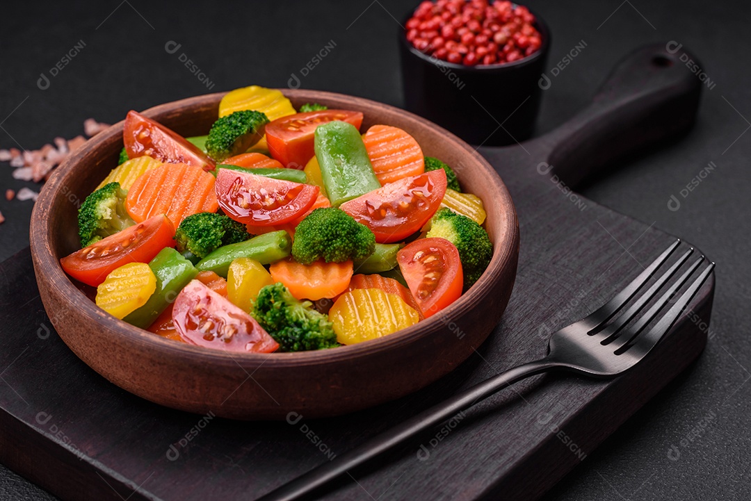 Salada de legumes frescos e cozidos no vapor, tomate cereja, brócolis, cenoura e feijão de espargos sobre um fundo escuro de concreto