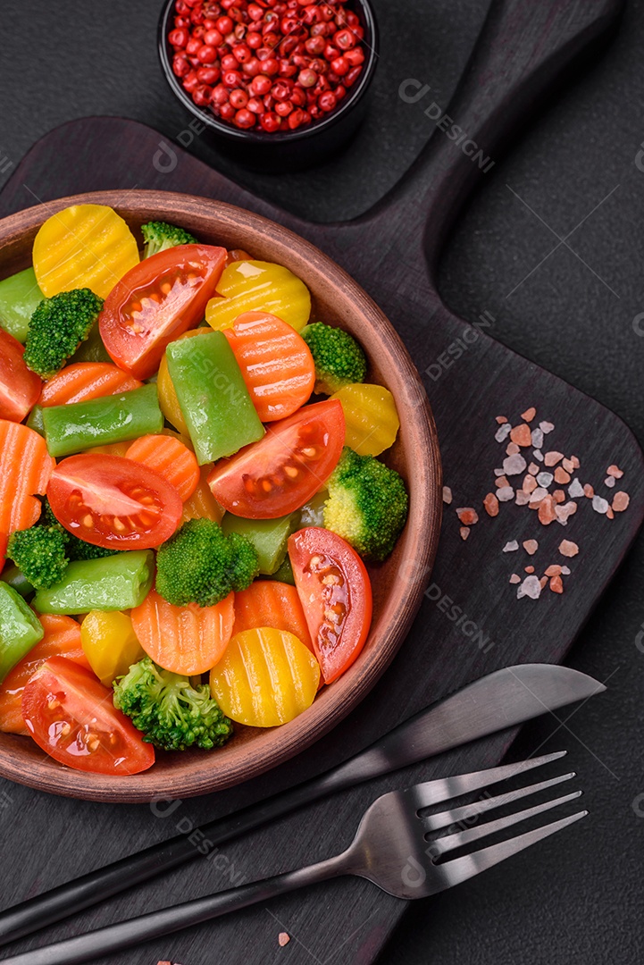Salada de legumes frescos e cozidos no vapor, tomate cereja, brócolis, cenoura e feijão de espargos sobre um fundo escuro de concreto
