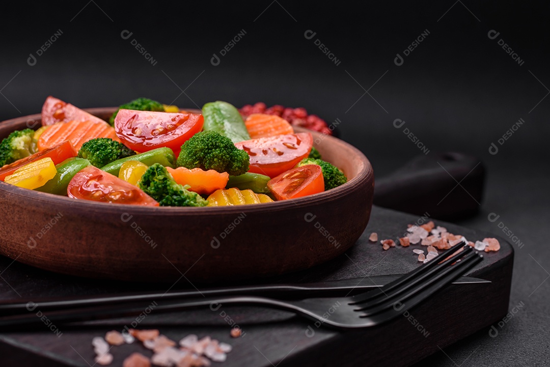Salada de legumes frescos e cozidos no vapor, tomate cereja, brócolis, cenoura e feijão de espargos sobre um fundo escuro de concreto