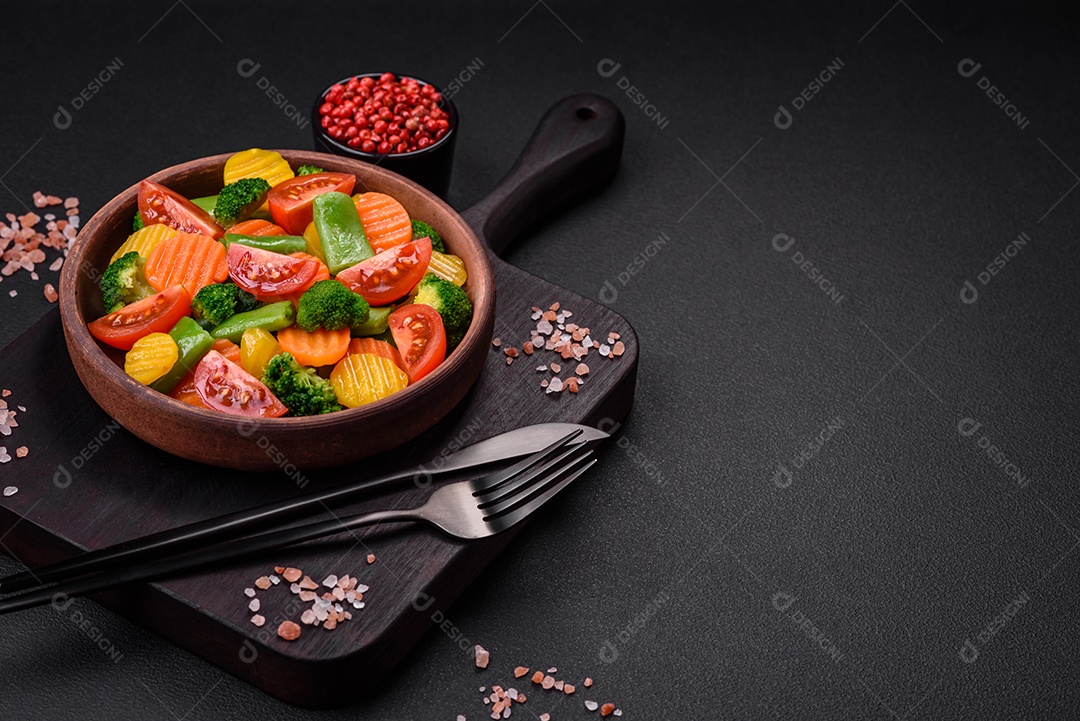 Salada de legumes frescos e cozidos no vapor, tomate cereja, brócolis, cenoura e feijão de espargos sobre um fundo escuro de concreto