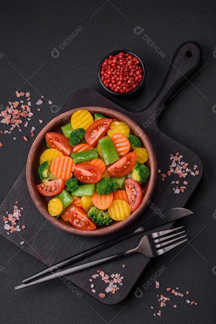 Salada de legumes frescos e cozidos no vapor, tomate cereja, brócolis, cenoura e feijão de espargos sobre um fundo escuro de concreto