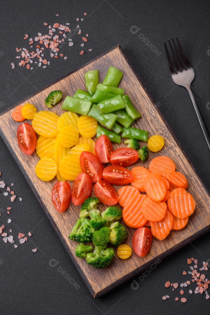 Salada de legumes frescos e cozidos no vapor, tomate cereja, brócolis, cenoura e feijão de espargos sobre um fundo escuro de concreto