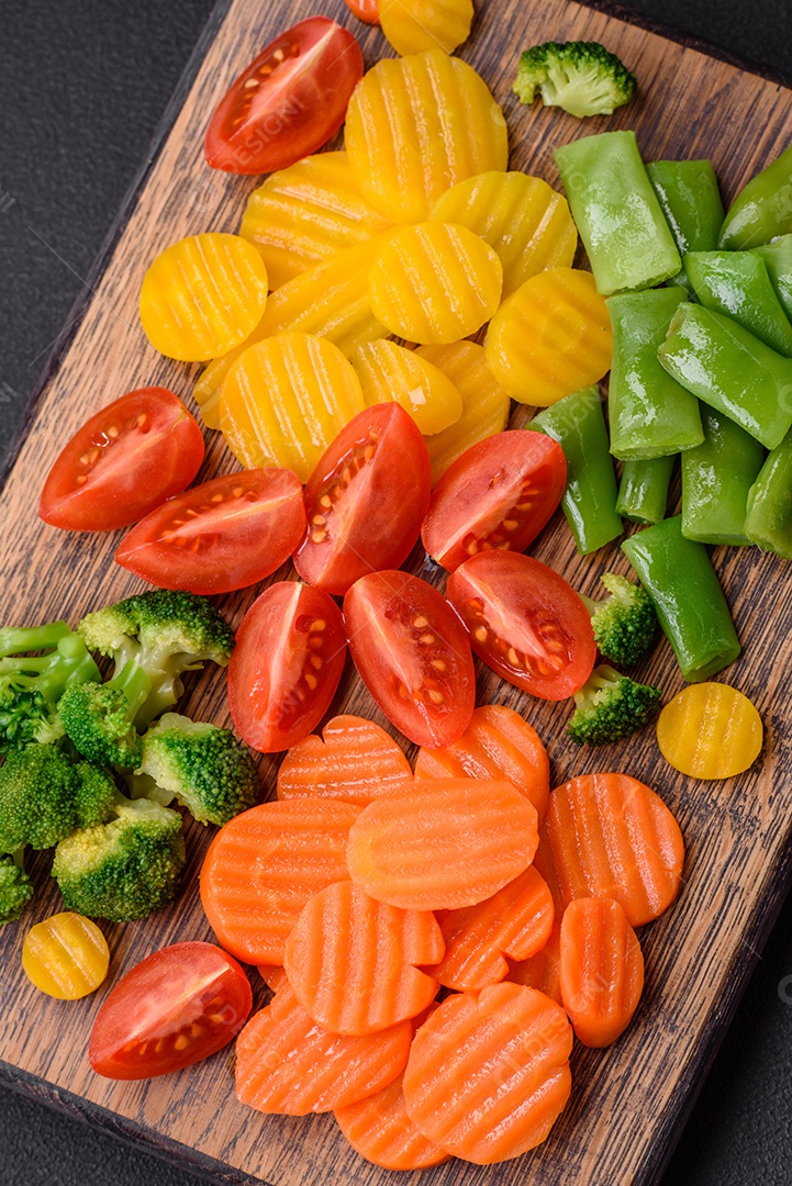 Salada de legumes frescos e cozidos no vapor, tomate cereja, brócolis, cenoura e feijão de espargos sobre um fundo escuro de concreto