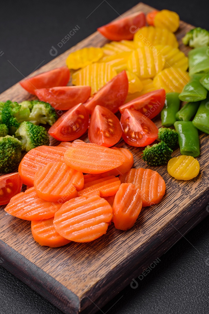 Salada de legumes frescos e cozidos no vapor, tomate cereja, brócolis, cenoura e feijão de espargos sobre um fundo escuro de concreto