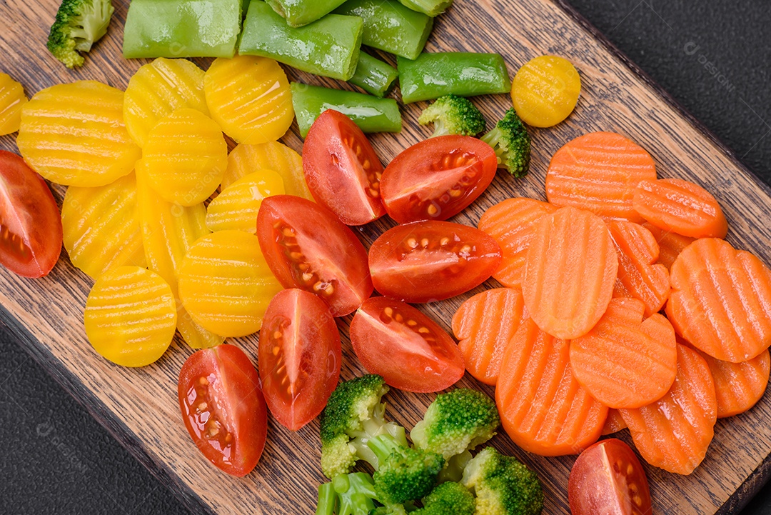 Salada de legumes frescos e cozidos no vapor, tomate cereja, brócolis, cenoura e feijão de espargos sobre um fundo escuro de concreto