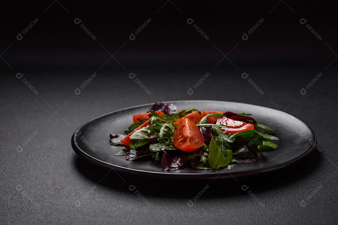 Salada de tomate cereja fresco, rúcula, espinafre, folhas jovens de beterraba e outras verduras sobre fundo escuro de concreto