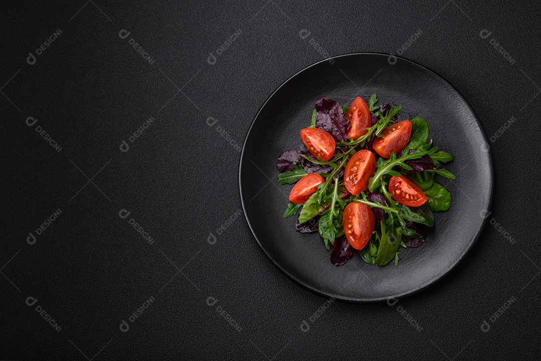 Salada de tomate cereja fresco, rúcula, espinafre, folhas jovens de beterraba e outras verduras sobre fundo escuro de concreto