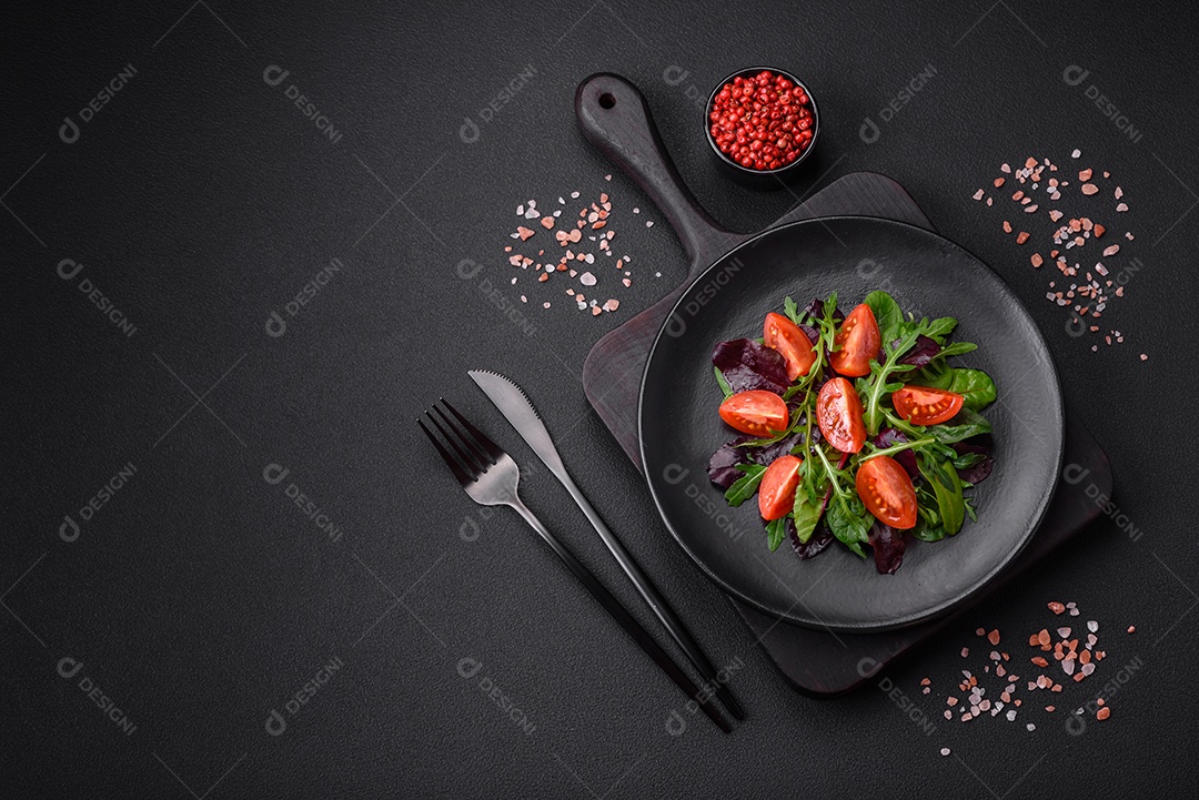 Salada de tomate cereja fresco, rúcula, espinafre, folhas jovens de beterraba e outras verduras sobre fundo escuro de concreto