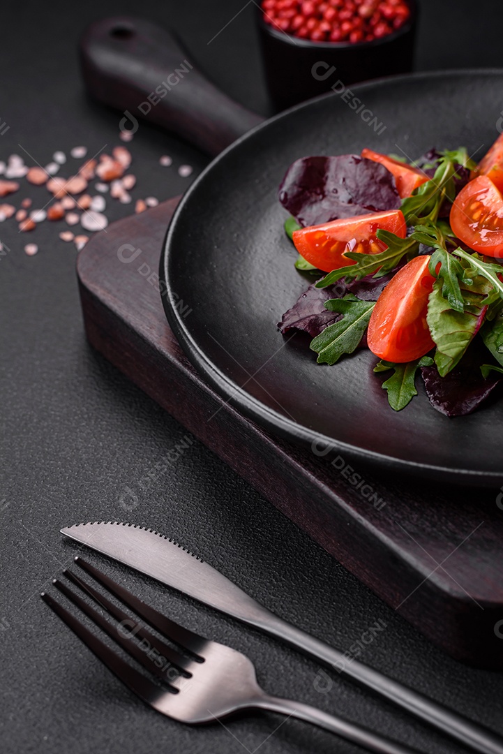 Salada de tomate cereja fresco, rúcula, espinafre, folhas jovens de beterraba e outras verduras sobre fundo escuro de concreto
