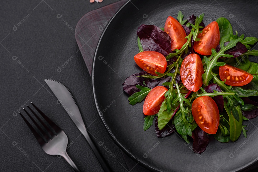 Salada de tomate cereja fresco, rúcula, espinafre, folhas jovens de beterraba e outras verduras sobre fundo escuro de concreto