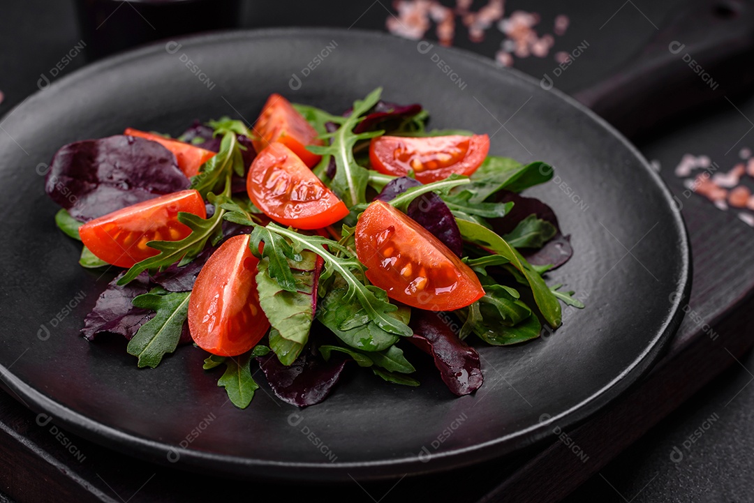 Salada de tomate cereja fresco, rúcula, espinafre, folhas jovens de beterraba e outras verduras sobre fundo escuro de concreto