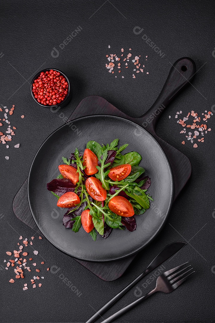 Salada de tomate cereja fresco, rúcula, espinafre, folhas jovens de beterraba e outras verduras sobre fundo escuro de concreto