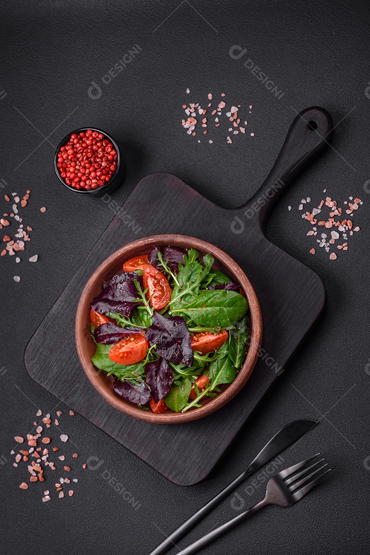 Salada de tomate cereja fresco, rúcula, espinafre, folhas jovens de beterraba e outras verduras sobre fundo escuro de concreto