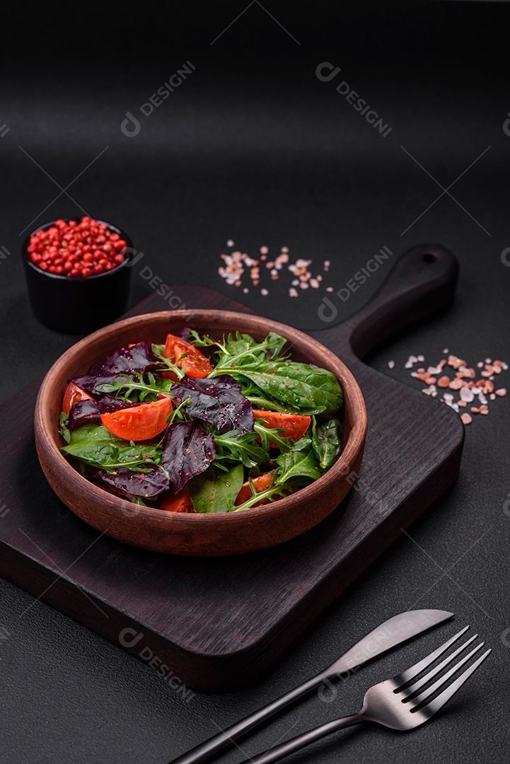 Salada de tomate cereja fresco, rúcula, espinafre, folhas jovens de beterraba e outras verduras sobre fundo escuro de concreto