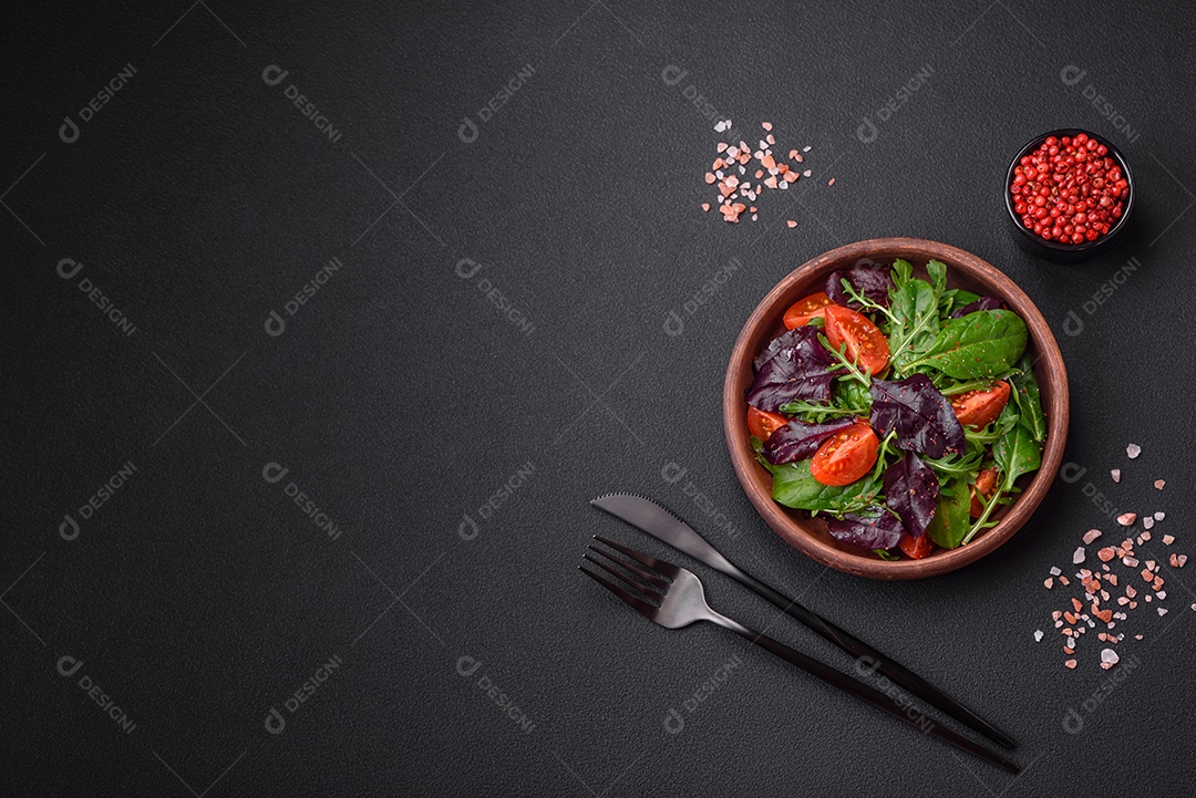 Salada de tomate cereja fresco, rúcula, espinafre, folhas jovens de beterraba e outras verduras sobre fundo escuro de concreto