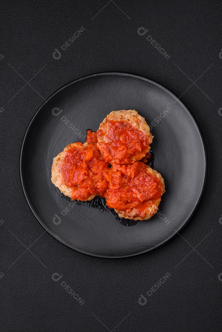 Deliciosas costeletas ou almôndegas frescas com especiarias, ervas e molho de tomate sobre um fundo escuro de concreto