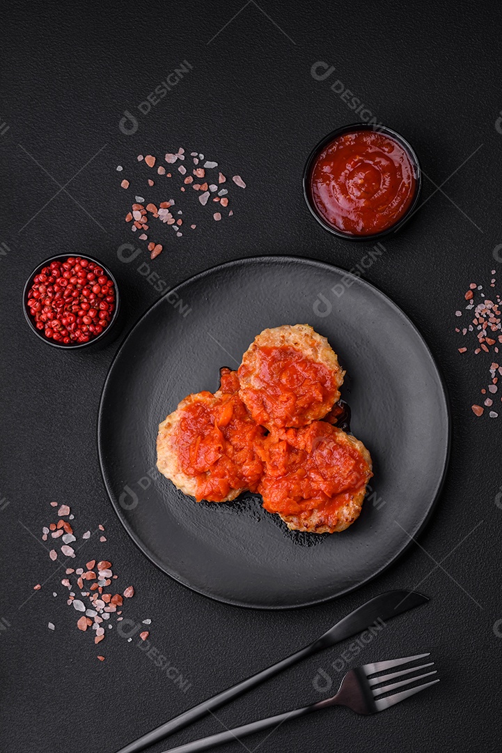 Deliciosas costeletas ou almôndegas frescas com especiarias, ervas e molho de tomate sobre um fundo escuro de concreto