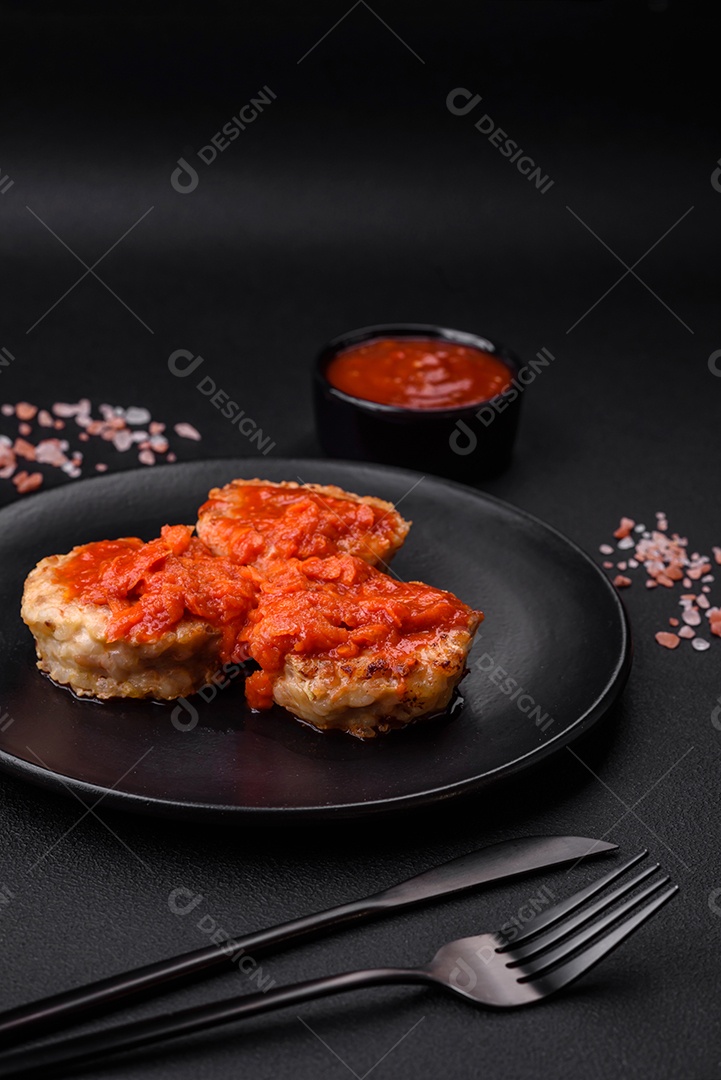 Deliciosas costeletas ou almôndegas frescas com especiarias, ervas e molho de tomate sobre um fundo escuro de concreto