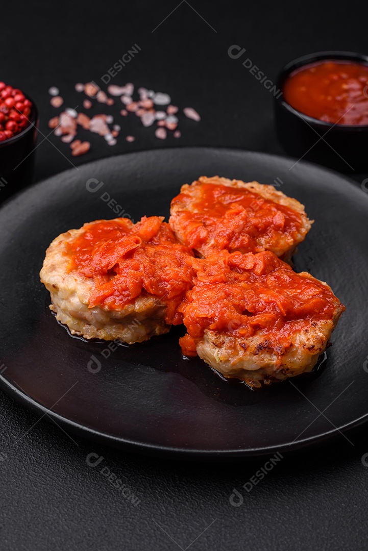 Deliciosas costeletas ou almôndegas frescas com especiarias, ervas e molho de tomate sobre um fundo escuro de concreto