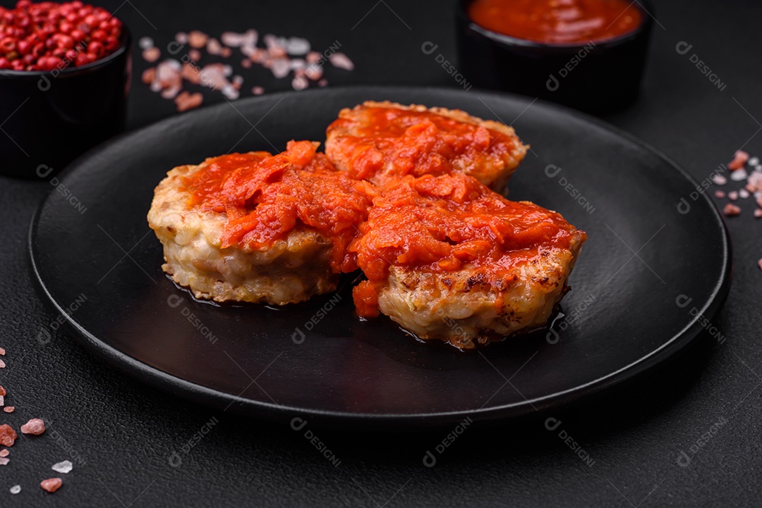 Deliciosas costeletas ou almôndegas frescas com especiarias, ervas e molho de tomate sobre um fundo escuro de concreto