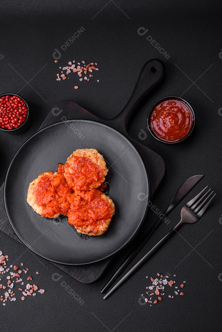 Deliciosas costeletas ou almôndegas frescas com especiarias, ervas e molho de tomate sobre um fundo escuro de concreto