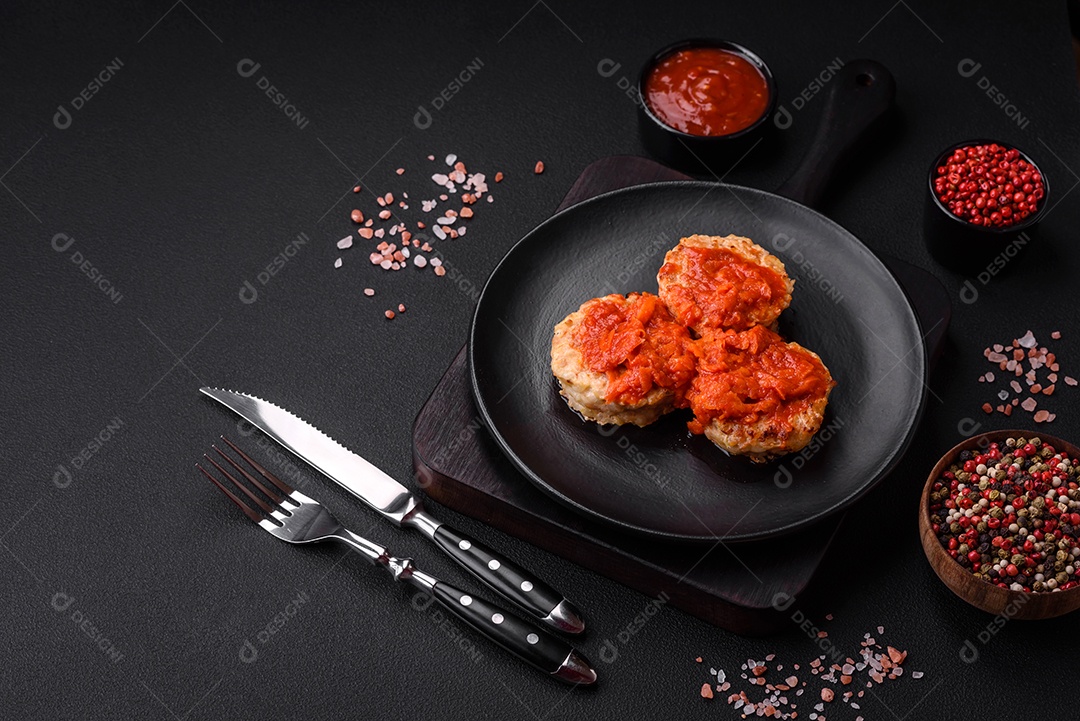 Deliciosas costeletas ou almôndegas frescas com especiarias, ervas e molho de tomate sobre um fundo escuro de concreto