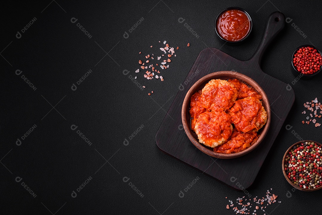 Deliciosas costeletas ou almôndegas frescas com especiarias, ervas e molho de tomate sobre um fundo escuro de concreto