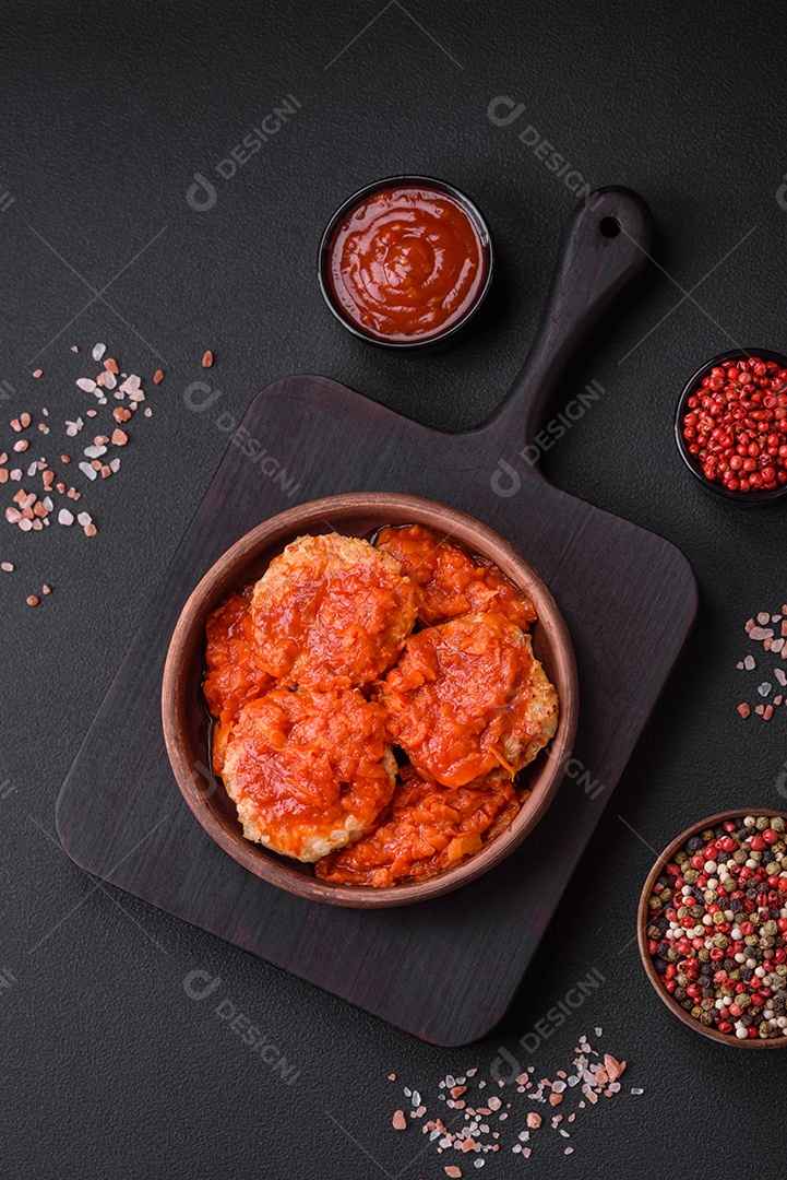 Deliciosas costeletas ou almôndegas frescas com especiarias, ervas e molho de tomate sobre um fundo escuro de concreto