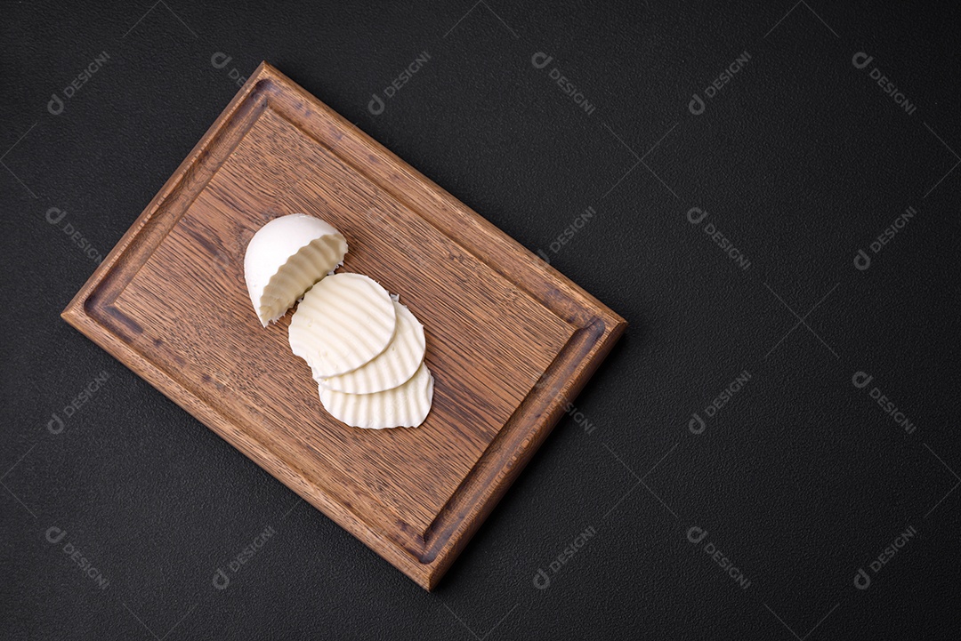 Deliciosa mussarela fresca cortada em fatias sobre uma tábua de madeira sobre um fundo escuro de concreto