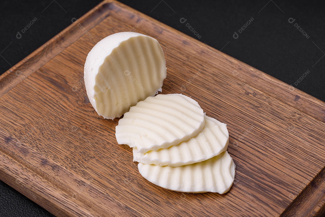 Deliciosa mussarela fresca cortada em fatias sobre uma tábua de madeira sobre um fundo escuro de concreto