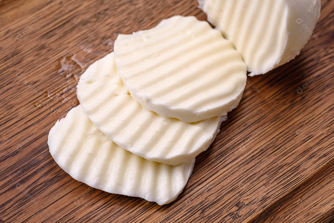 Deliciosa mussarela fresca cortada em fatias sobre uma tábua de madeira sobre um fundo escuro de concreto