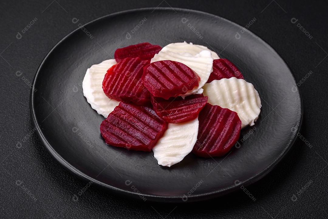 Deliciosa mussarela fresca e beterraba cozida cortada em fatias em uma placa cerâmica redonda sobre um fundo escuro de concreto