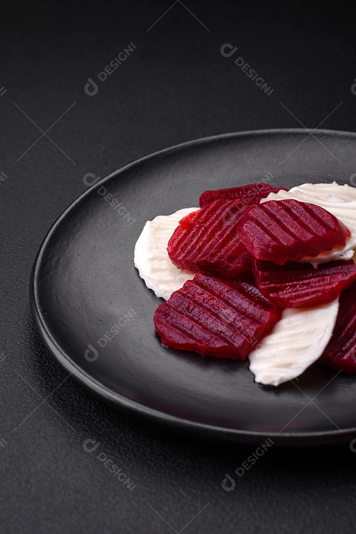 Deliciosa mussarela fresca e beterraba cozida cortada em fatias em uma placa cerâmica redonda sobre um fundo escuro de concreto