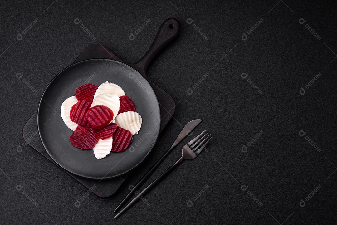 Deliciosa mussarela fresca e beterraba cozida cortada em fatias em uma placa cerâmica redonda sobre um fundo escuro de concreto