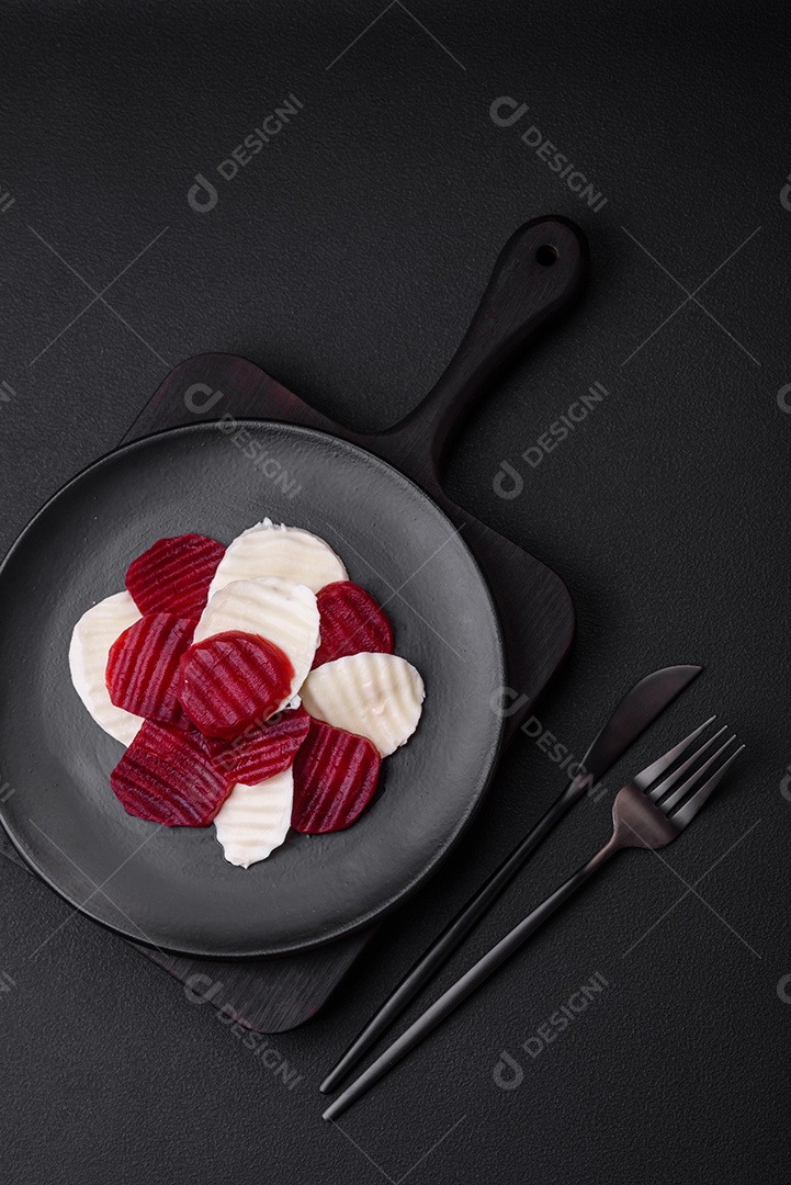 Deliciosa mussarela fresca e beterraba cozida cortada em fatias em uma placa cerâmica redonda sobre um fundo escuro de concreto