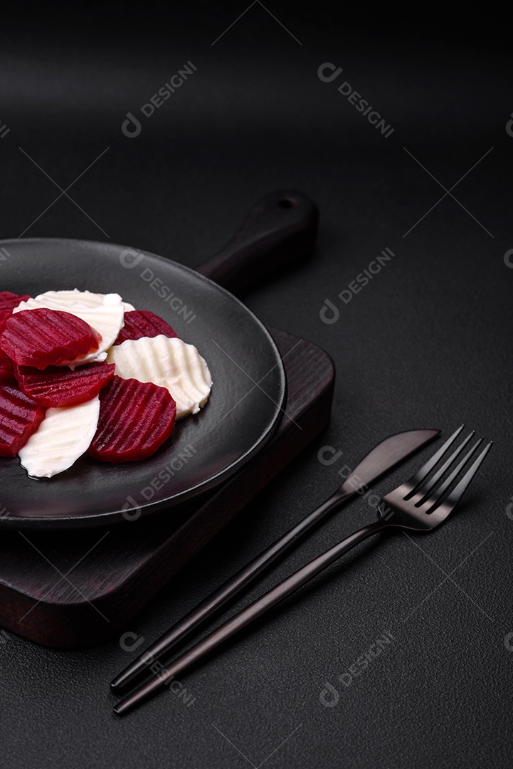 Deliciosa mussarela fresca e beterraba cozida cortada em fatias em uma placa cerâmica redonda sobre um fundo escuro de concreto