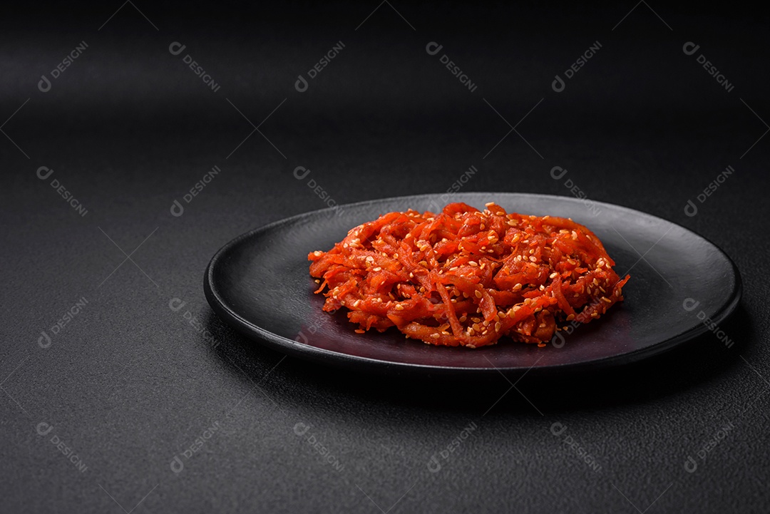 Lulas secas cortadas em fatias e temperadas com sementes de gergelim e especiarias sobre fundo escuro de concreto. Prato da culinária coreana