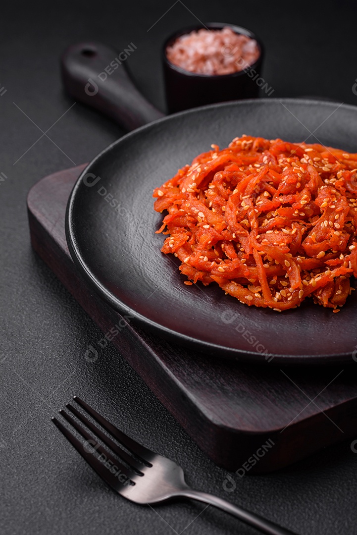 Lulas secas cortadas em fatias e temperadas com sementes de gergelim e especiarias sobre fundo escuro de concreto. Prato da culinária coreana