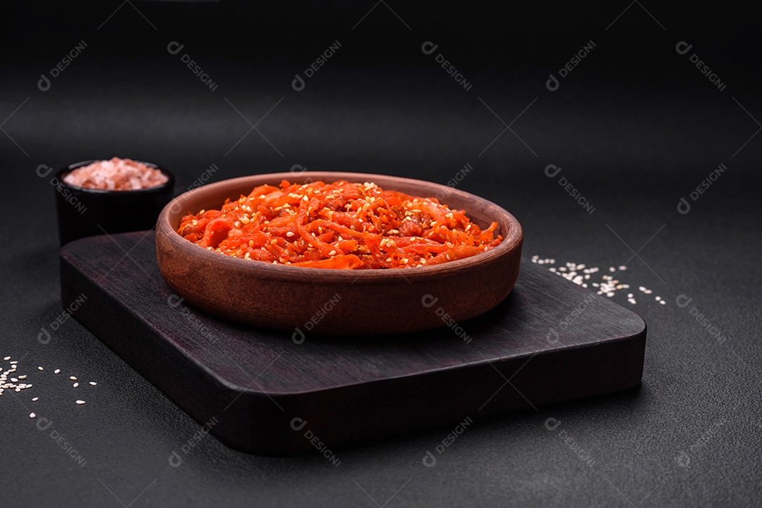 Lulas secas cortadas em fatias e temperadas com sementes de gergelim e especiarias sobre fundo escuro de concreto. Prato da culinária coreana