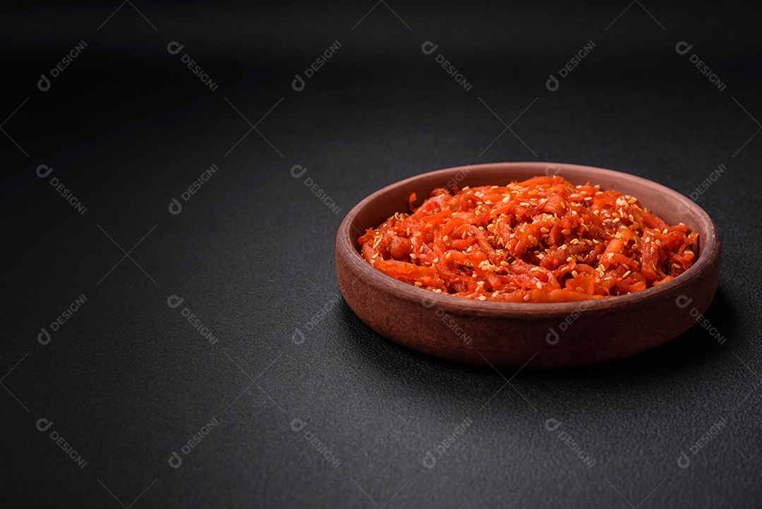 Lulas secas cortadas em fatias e temperadas com sementes de gergelim e especiarias sobre fundo escuro de concreto. Prato da culinária coreana