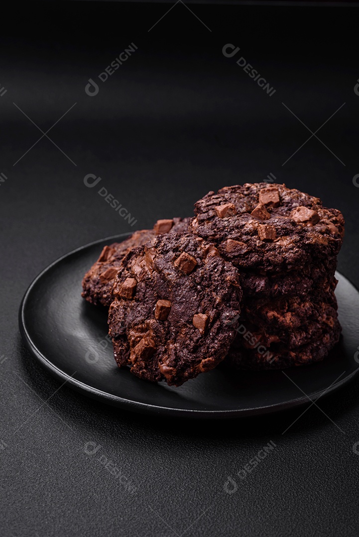 Deliciosos biscoitos de aveia crocantes e frescos com chocolate e nozes em uma placa de cerâmica preta sobre um fundo escuro de concreto