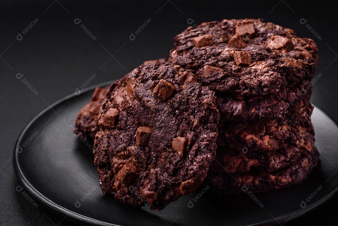 Deliciosos biscoitos de aveia crocantes e frescos com chocolate e nozes em uma placa de cerâmica preta sobre um fundo escuro de concreto