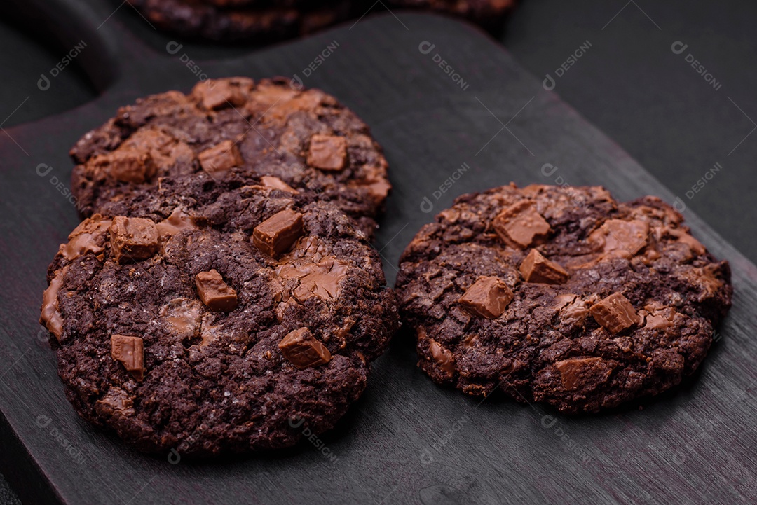 Deliciosos biscoitos de aveia crocantes e frescos com chocolate e nozes em uma placa de cerâmica preta sobre um fundo escuro de concreto