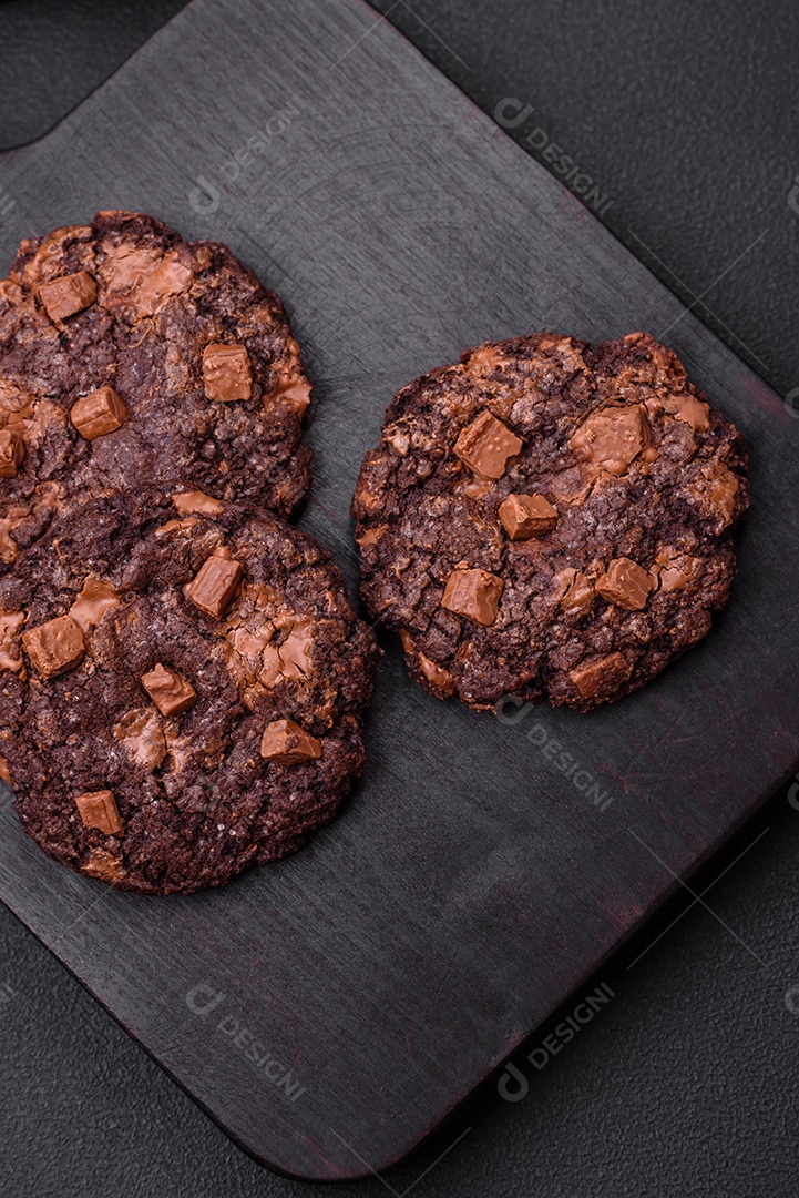 Deliciosos biscoitos de aveia crocantes e frescos com chocolate e nozes em uma placa de cerâmica preta sobre um fundo escuro de concreto