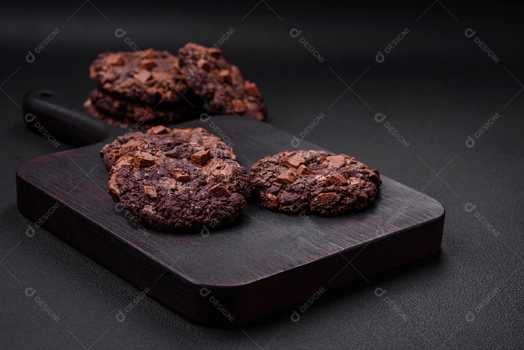 Deliciosos biscoitos de aveia crocantes e frescos com chocolate e nozes em uma placa de cerâmica preta sobre um fundo escuro de concreto