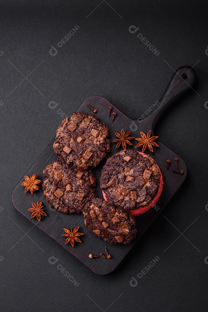 Deliciosos biscoitos de aveia crocantes e frescos com chocolate e nozes em uma placa de cerâmica preta sobre um fundo escuro de concreto