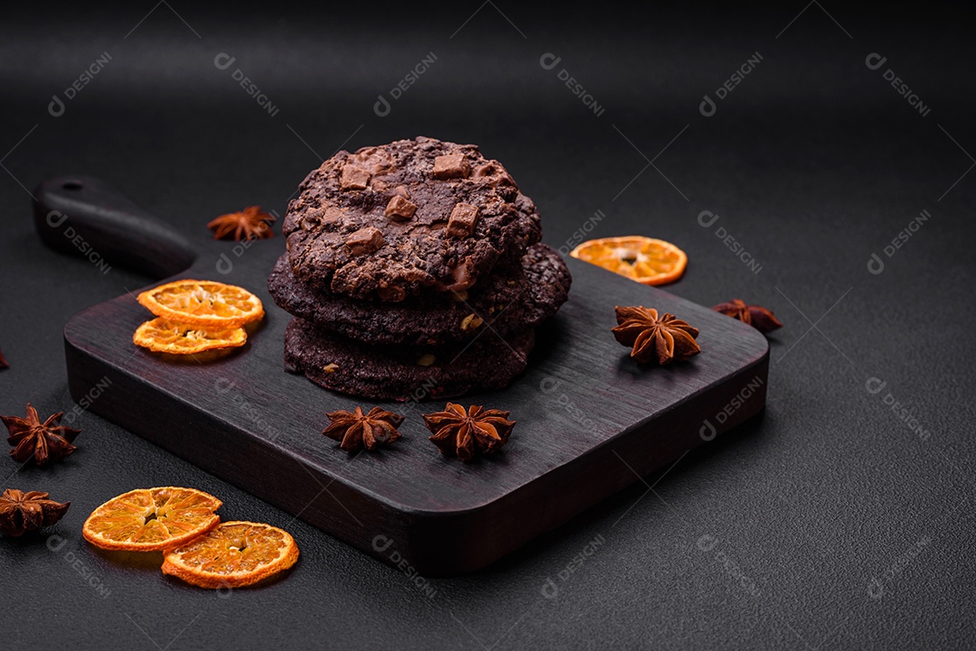 Deliciosos biscoitos de aveia crocantes e frescos com chocolate e nozes em uma placa de cerâmica preta sobre um fundo escuro de concreto