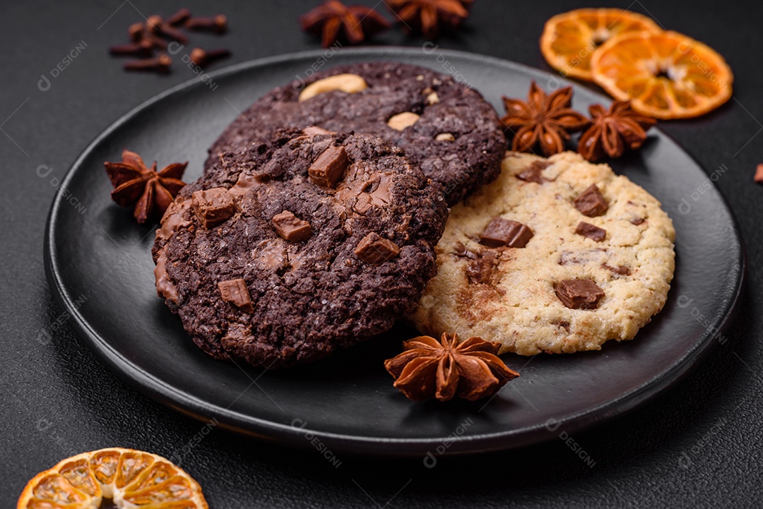 Deliciosos biscoitos de aveia crocantes e frescos com chocolate e nozes em uma placa de cerâmica preta sobre um fundo escuro de concreto