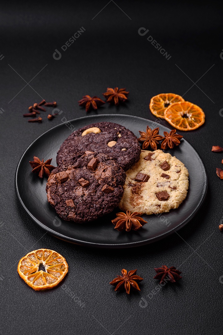 Deliciosos biscoitos de aveia crocantes e frescos com chocolate e nozes em uma placa de cerâmica preta sobre um fundo escuro de concreto